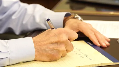 A close-up of hands writing with a pen on a legal pad
